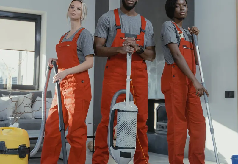Professional cleaning crew in uniform with a vacuum and mop in a modern home