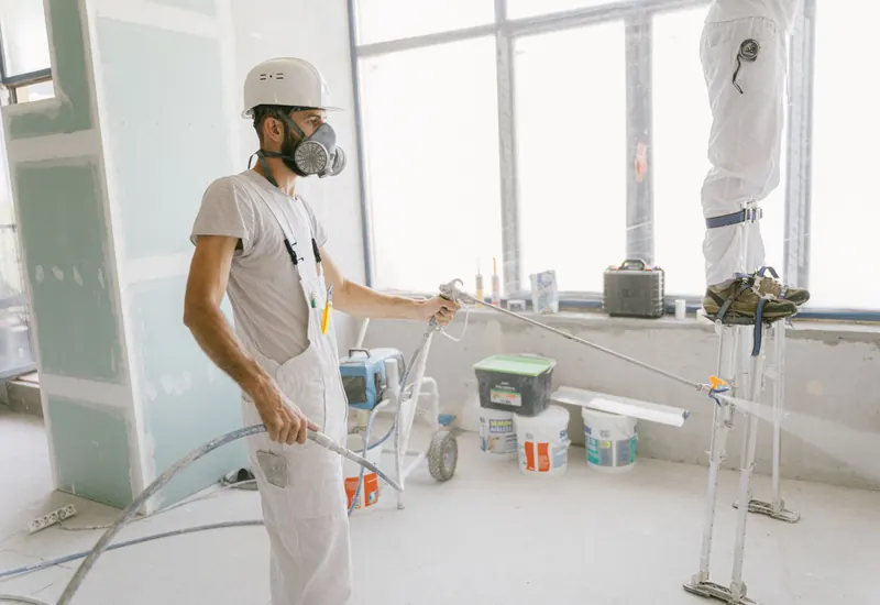 Painter in protective gear spray-painting an interior wall